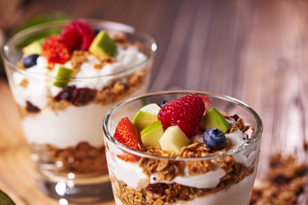 Close-up view of two glasses of delicious yogurt and fruits including strwaberries, kiwi, blueberry ontop for health on wooden tableの写真素材