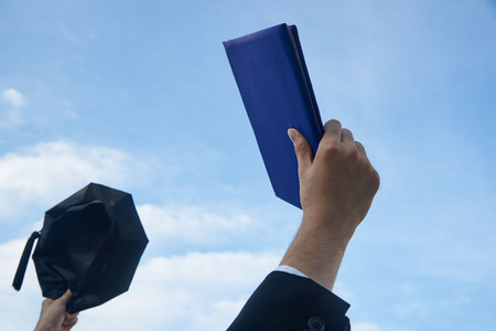 A graduate raising the degree and graduate hat up in the air