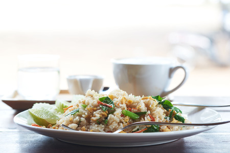 A plate of delicious fried rice and a tasty cup of latte coffee on wooden tableの写真素材