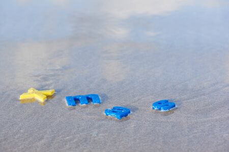 Merry Christmas. Letter in different colors on the sand and sea waves with morning sunlight and...