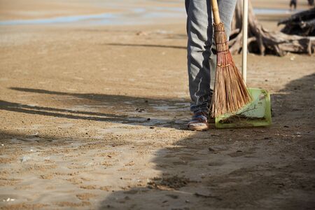 A worker using broom sweeping the trash on the beach in the morningの写真素材