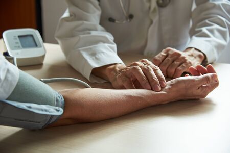 A male doctor examining a female patient pulse rate with digital sphygmomanometer wrapping around the arm in medical office.の写真素材