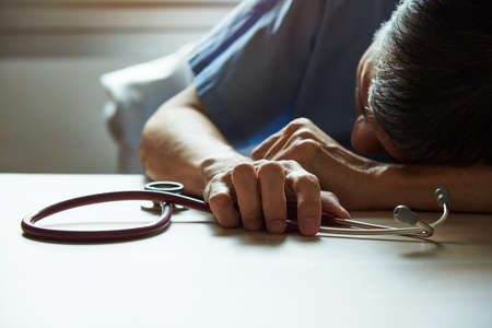 An asian burnout surgeon feeling tired in medical office with a stethoscope on the tableの写真素材