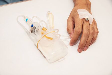 Close-up view of patient  with heparin lock needle in the vein of left hand. Used bag of antibiotic...
