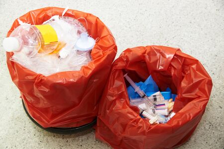 Used bottle of medications, syringes, endotracheal tube, bottle of urine in two red garbage bins for biohazard disposalの写真素材