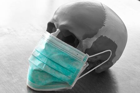 A human skull model in black and white wearing green facial mask for viral infection protectionの写真素材