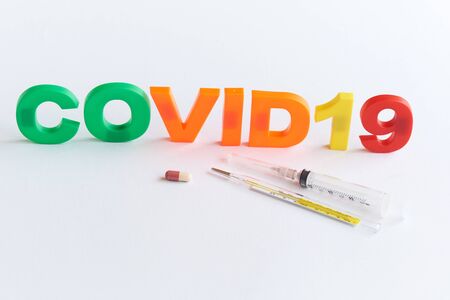A capsule of medication, thermometer and syringe with needle on white background with covid-19...