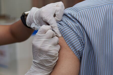 A nurse injecting  a dose of influenza vaccine at patient armの写真素材
