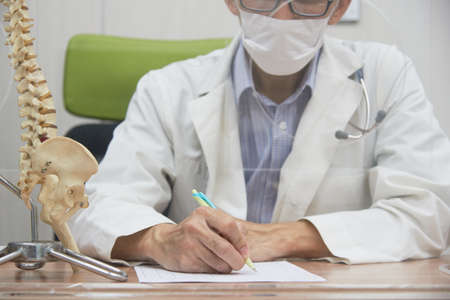 A male asian doctor writing prescription in medical office. New normal of clinic for coronavirus or covid-19 protection.の写真素材
