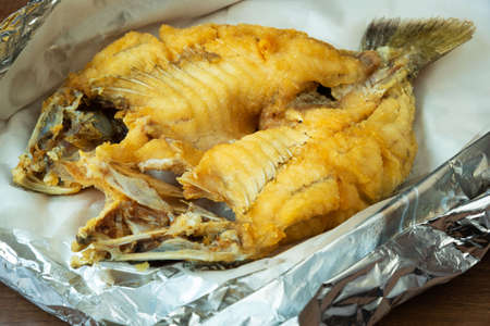 Hot fried snapper topped with sauce on a plate with foil paper