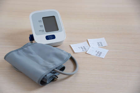Paper showing blood pressure number and automatic sphygmomanometer on the table