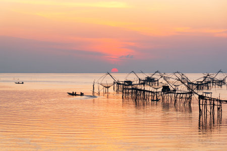 Sunrise and silhouette image of tourists on long tail boat and giant fishing net in the morning at Pakpra, Phatthalung, Thailand.の写真素材