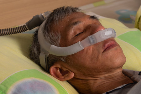 An Asian oder male asleep with CPAP machine for sleep apnea treatment in a home setting