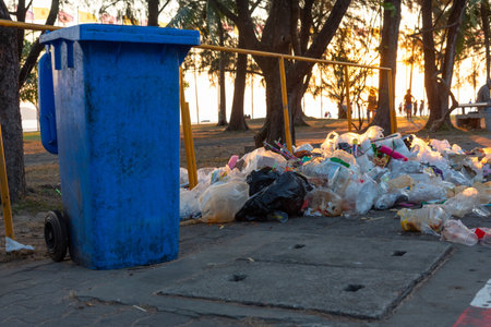 A large pile of plastic waste and litter accumulated near a blue trash bin in a park, illustrating the aftermath of a New Year celebration. The scene highlights environmental pollution and the need for responsible waste management.の写真素材