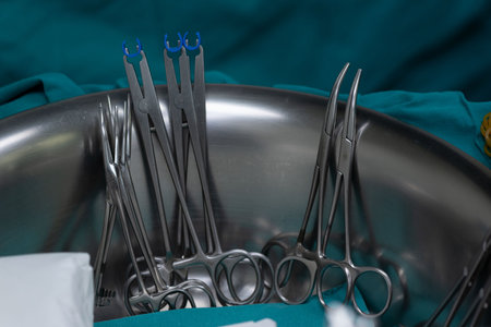 A Surgical clamps and forceps in stainless steel bowl on medical drape, prepared for medical procedureの写真素材
