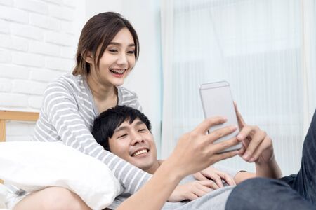 Asian Couple or lover in love using phone on the bed.の写真素材