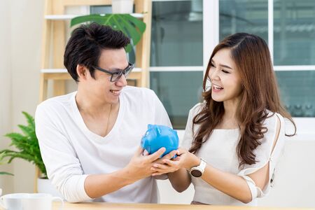 Young happy asian couple smile ,looking each other and holding piggy bank. Saving and happy family concept.の写真素材