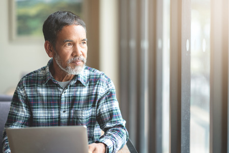 Mature man with white stylish short beard looking outside window. Casual lifestyle of retired...