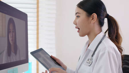 Attractive beautiful asia chinese female doctor video conference call online live talk follow up remotely in medical coronavirus result with patient at office. Online telehealth telemedicine service.の写真素材