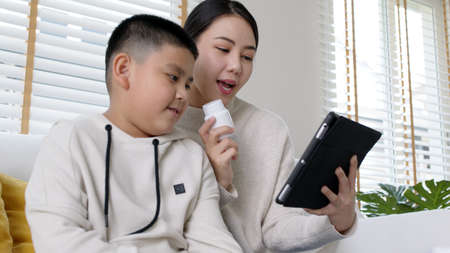 Young asia parents and son talk to doctor on cellphone videocall conference medical app in pediatric...