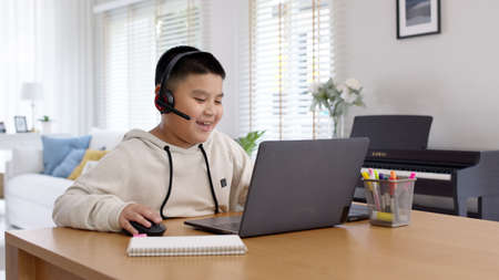 Young asia boy student wear headset headphone with computer laptop videocall talk present online e-learning class study with teacher, social distance learn language at home, homeschooling concept.の写真素材