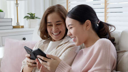 Attractive beautiful asian family sit sofa couch living room enjoy urban life joyful promotion discount shop buy health care insurance online quarantine activity isolate omnichannel experience at homeの写真素材