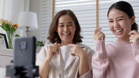 Candid mum and grown kid sit sofa couch at home living room enjoy benefit quarantine self isolate activity in coronavirus covid. Family enjoy selfie filming record by internet network wifi connection.の写真素材