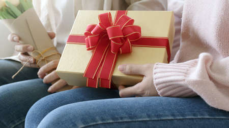 Attractive beautiful asian middle age mum sit with grown up daughter give gift box and flower in...