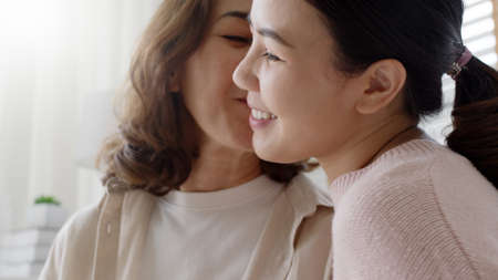 Attractive beautiful asian middle age mum sit with grown up daughter give gift box and flower in family moment celebrate mother day. Overjoy bonding cheerful kid embrace relationship with retired mom.の写真素材