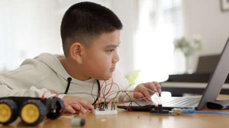 Young asia student remotely learn online at home in coding robot car and electronic board cable in STEM, STEAM, mathematics engineering science technology computer code in robotics for kids concept.の写真素材