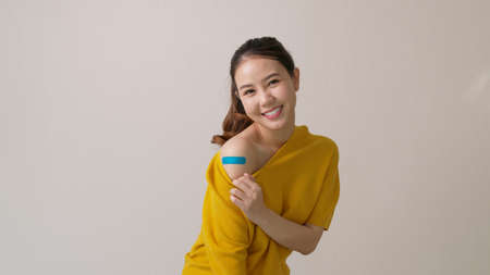 Young attractive beautiful asia female or teenage receive covid-19 anti virus vaccine in campaign vaccination safe life happy smile cheerful with blue, yellow, pink bandage on arm with copy space.の写真素材