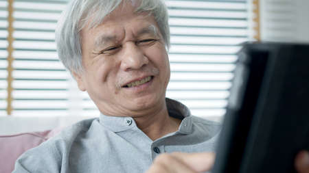 Candid old asian retired guy use tablet computer to transfer money online or financial payment and...