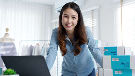 Portrait young attractive asia female owner startup business look at camera work happy with box at...