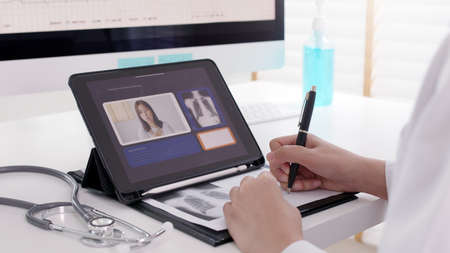 Attractive beautiful asia   female doctor video conference call online live talk follow up remotely in medical coronavirus result with patient at office. Online telehealth telemedicine service.の写真素材