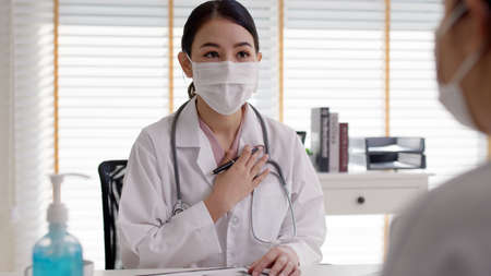 Attractive beautiful young asia female wear surgical mask white gown stethoscope on shoulders diagnosis talk to sick patient provide help counseling consult, therapy or explain prescribe in clinic.の写真素材