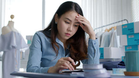 Young attractive asia female business owner thoughtful serious doubtful feel stress worry with financial problem in SME crisis small business challenges impact from covid coronavirus at home office.の写真素材