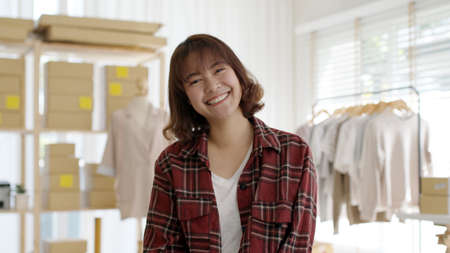 Portrait young attractive asia female owner startup business look at camera work happy with carton box at home prepare delivery in sme supply chain, procurement, omnichannel ecommerce online concept.の写真素材