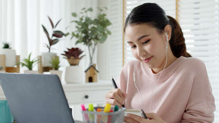 Cozy relax young attractive asian female employee wear earphone listen to digital online course...