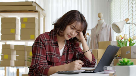 Young attractive asia female hipster thoughtful serious doubtful feeling stress worry with financial problem in SME crisis small business challenges impact from covid coronavirus at home office.の写真素材
