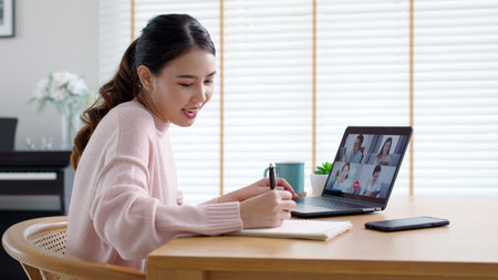 Back view of business woman talking about sale report in video conference. Asian team using laptop and tablet online meeting in video call.Working from home, Working remotely and Social isolation.の写真素材