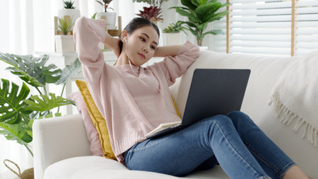 Cozy relax young attractive asian female employee wear earphone listen to digital online course development program in quarantine social distance at home reskill upskill school class for career path.の写真素材