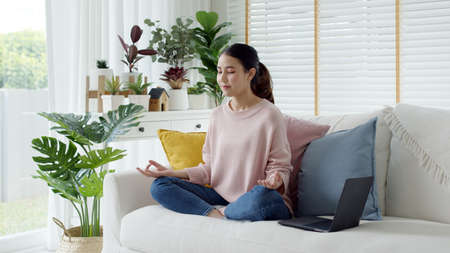 Attractive beautiful young asia female close eyes maditate at home self break stress relief from work, stay quarantine social distance in online yoga class community, wellness wellbeing lifestyle.の写真素材