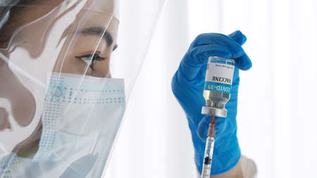 Close up hand of doctor or researcher with face mask holding and filling up a vaccine to syringe. Medical with face mask filling a syringe with vaccine. Covid19 coronavirus vaccine in a syringe.の写真素材