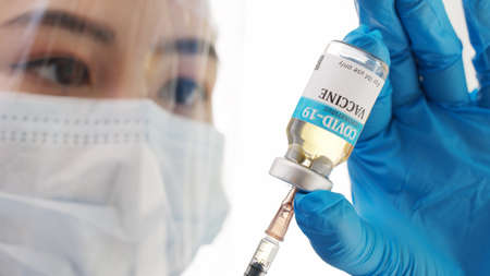 Close up hand of doctor or researcher with face mask holding and filling up a vaccine to syringe. Medical with face mask filling a syringe with vaccine. Covid19 coronavirus vaccine in a syringe.の写真素材