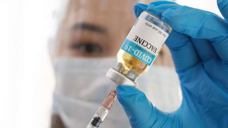 Close up hand of doctor or researcher with face mask holding and filling up a vaccine to syringe. Medical with face mask filling a syringe with vaccine. Covid19 coronavirus vaccine in a syringe.の写真素材
