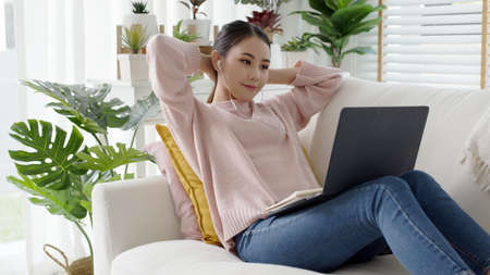 Cozy relax young attractive asian female employee wear earphone listen to digital online course development program in quarantine social distance at home reskill upskill school class for career path.の写真素材