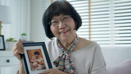 Portrait of happy senior asian woman relax sitting smile looking at photo frame reminding the past...