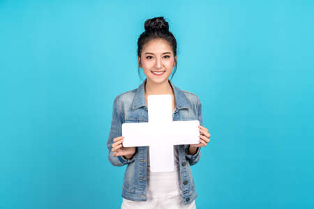 Happy asian woman standing and holding plus or add sign on blue background. Cute asia girl smiling...