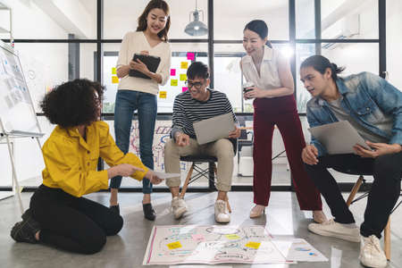 Young creative asian group meeting and looking at project plan lay out on floor discuss or...