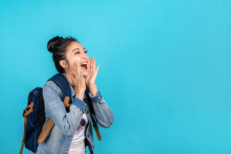 Happy asian woman travel backpacker shouting open mouth to copyspace on blue background. Cute asia...